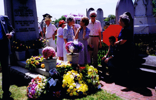 Figures standing by gravestone that is covered in floral wreaths
