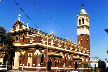 Brown brick building with white cement ornamentation and a grey slate roof. The bell tower has a green roof.