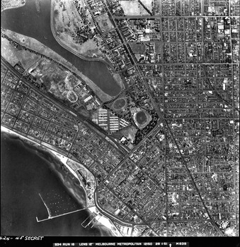 Rooftops, roads, trees, open spaces and shoreline seen from the air directly above.