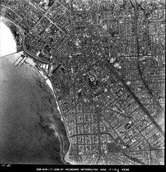 Rooftops, roads, trees, open spaces and shoreline seen from the air directly above.