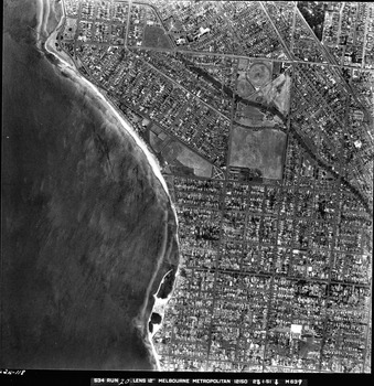 Rooftops, roads, trees, open spaces and shoreline seen from the air directly above.
