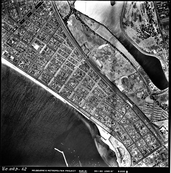 Rooftops, roads, trees, open spaces and shoreline seen from the air directly above.