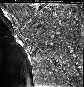 Rooftops, roads, trees, open spaces and shoreline seen from the air directly above.