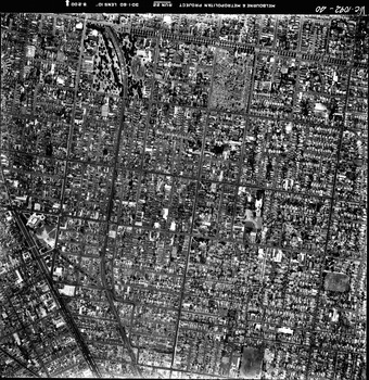 Rooftops, roads, trees and open spaces seen from the air directly above.
