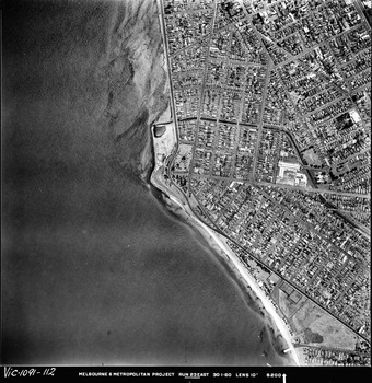 Rooftops, roads, trees, open spaces and shoreline seen from the air directly above.