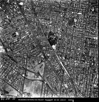 Rooftops, roads, trees and open spaces seen from the air directly above.