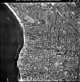 Rooftops, roads, trees, open spaces and shoreline seen from the air directly above.