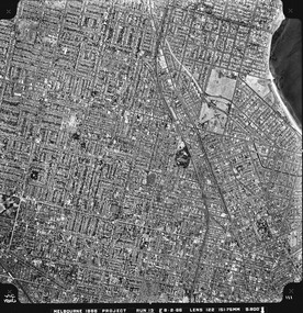 Rooftops, roads, trees, open spaces and shoreline seen from the air directly above.