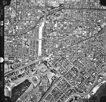 Rooftops, roads, trees, open spaces and shoreline seen from the air directly above.