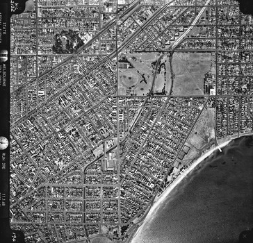 Rooftops, roads, trees, open spaces and shoreline seen from the air directly above.