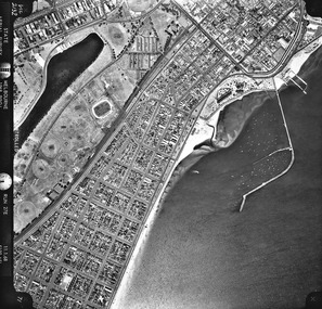 Rooftops, roads, trees, open spaces and shoreline seen from the air directly above.