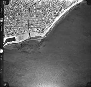 Rooftops, roads, trees, open spaces and shoreline seen from the air directly above.