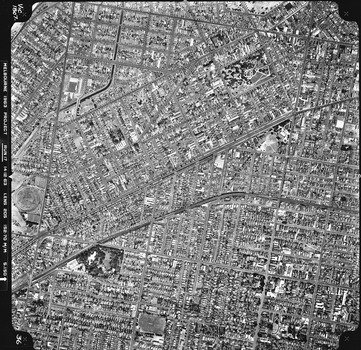 Rooftops, roads, trees and open spaces seen from the air directly above.