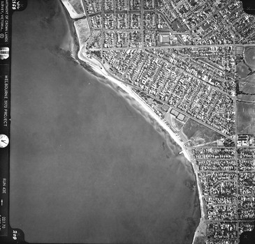 Rooftops, roads, trees, open spaces and foreshore seen from the air directly above.
