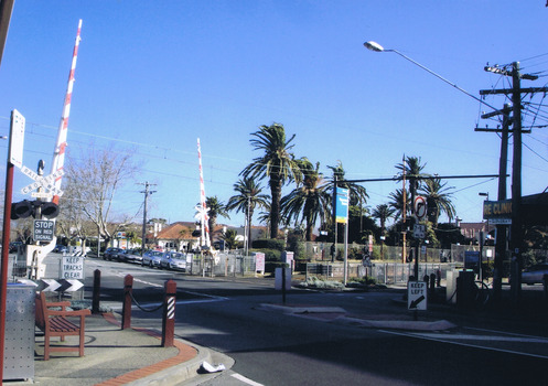 A railway crossing on an empty road. The boom gates are up.