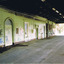 An empty, disused, station platform, covered by a wooden roof. The brick walls of the station building are painted with graffiti.