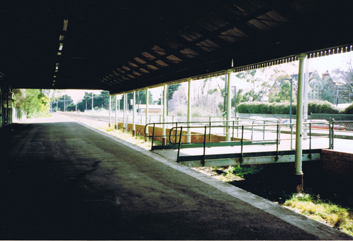 An empty, disused, station platform, covered by a wooden roof. 