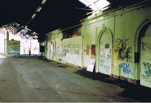 An empty, disused, station platform, covered by a wooden roof. The brick walls of the station building are painted with graffiti.