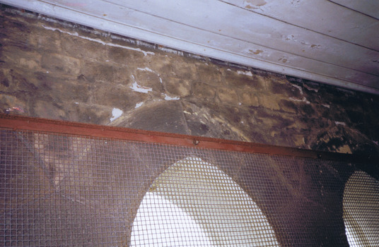 Stone windows covered in rusty wire mesh