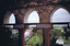 Playing fields and buildings seen from a height through arched stone windows covered in rusty wire mesh