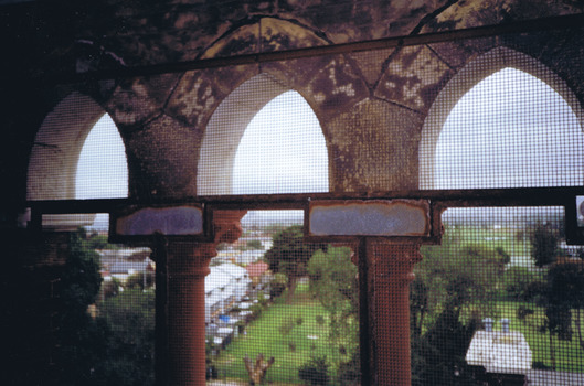 Playing fields and buildings seen from a height through arched stone windows covered in rusty wire mesh