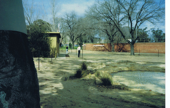 A muddy pond in cleared land. Two men observe in the distance.