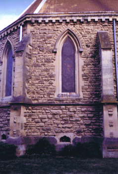 Two pointed arch windows, in two of the three stone walls that form the apse of the church. A supporting buttress is on each side.