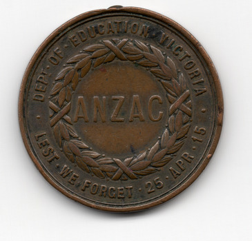 Circular brown medallion with words around the circumference Dept of Education Victoria Lest We Forget 25 Apr 15. In the centre a wreath surrounds the word ANZAC. 