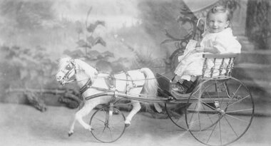 Photograph, Baby in a Wheeled Cart drawn by a toy horse -- Studio Portrait