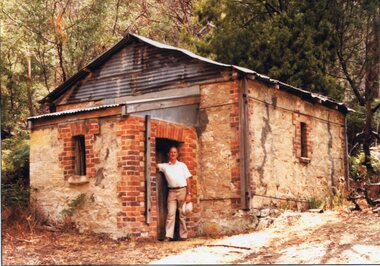 Photograph, Heatherlie Quarry with Geoff Sudholz standing in doorway of the stone building -- Coloured