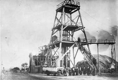 Photograph, Char-A-Banc belonging to Withers Bus Tours with a group of people in front of Sloane's & Scotchman Mining Co's Poppet Head c 1920
