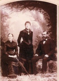 Photograph, Studio Portrait of two women and man.  One lady has umbrella