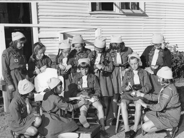 Photograph, Group off brownies doing first aid activities outside building
