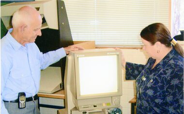 Photograph, Two people in library next to a Microfische