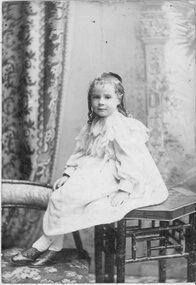 Photograph, Young girl in smock seated on table in studio portrait