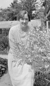 Photograph, Marjorie Cragg in garden with flowering bush