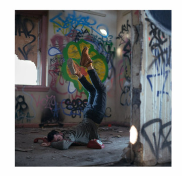 This photograph is taken at the site of the ruins of an old asylum in Bundoora, graffiti covers the walls and light filters in through a broken window on the left.  This is a place of solitude for the artist.  In this self-portrait the artist is pictured precariously balancing on his chest while his legs are floating in the air.  He holds onto an old style red telephone receiver that appears to anchor him to the ground.  
