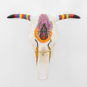 A 3D printed bull skull with horns painted in vibrant blue, red and  yellow stripes and black painted tips, and a redback spider painted on the centre of the skull.  A small crucifix is attached to the redback spider and beaded jewellery is looped through the eyes of the skull.