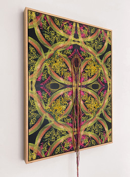 The work has a symmetrical print with green and red coloured leaf shapes featured as its base. There are elements of embroidery of yellow wattle like flowers stitched onto the surface of the prints. There is bright pink stitching on the surface as well. Coloured floss twine is also attached on the surface of the work that hangs down beyond the dimension of the frame at the bottom of the work