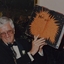 A large book open to an artwork page being held up by a man standing at a microphone.
