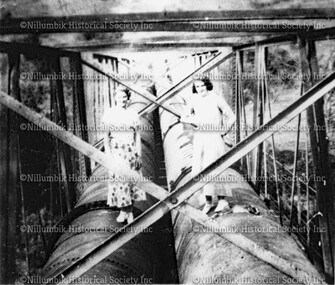 Two ladies standing on pipeline over Plenty River