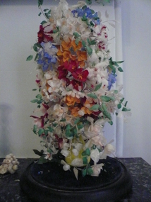 Glass dome on wooden base enclosing a floral display made entirely of dyed fish scales.