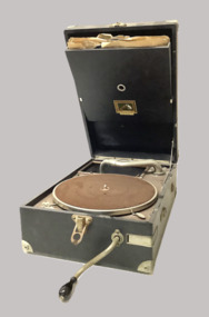 Portable winding gramaphone. Dark brown case with hinged lid. Includes two records (78’s - bakelite) stored in the lid.