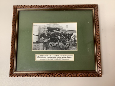 Framed photo of Hugo Kretzschmar, blacksmith farrier and coachmaker, standing in front of a two wheeled cart in Newport