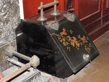 Coal scuttle, black painted metal, decorated with a painted gold holly spray and red berries. Brass handle, four brass feet and brass pull knob, opening at front with brass hinges.  Removable tray, containing a poker.  
