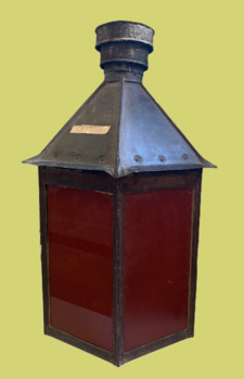 Kerosene burning pier lamp/light. Six sided metal lamp housing with glass inserts on all six sides, three plain and three red painted.  A side hinged door provides access to the lamp.  Detachable breathing chimney painted black.
