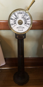 Engine-room telegraph - comprising a large cast iron pedestal on which is mounted a circular white enamelled brass instrument face. A lever on the side of the dial can be moved to indicate changes of course. 