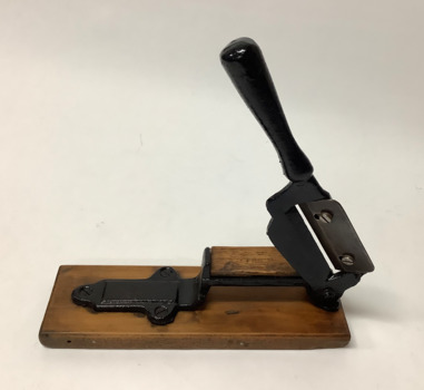 Cleaver shaped tobacco cutter with a metal handle and off-set sharpened blade (secured by two set screws) protruding through a slot. 