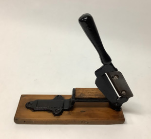 Cleaver shaped tobacco cutter with a metal handle and off-set sharpened blade (secured by two set screws) protruding through a slot. 