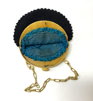 Small circular black cotton crocheted evening handbag, with a cream plastic clasp and a plastic chain link handle. The clasp has a design of four elephants and a depiction of Buddha in the centre. Peacock blue coloured silk lining, with ruched edging.
